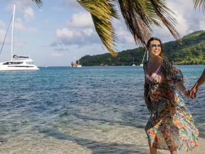 Couple walking on a beach in Tahiti with catamaran in the background